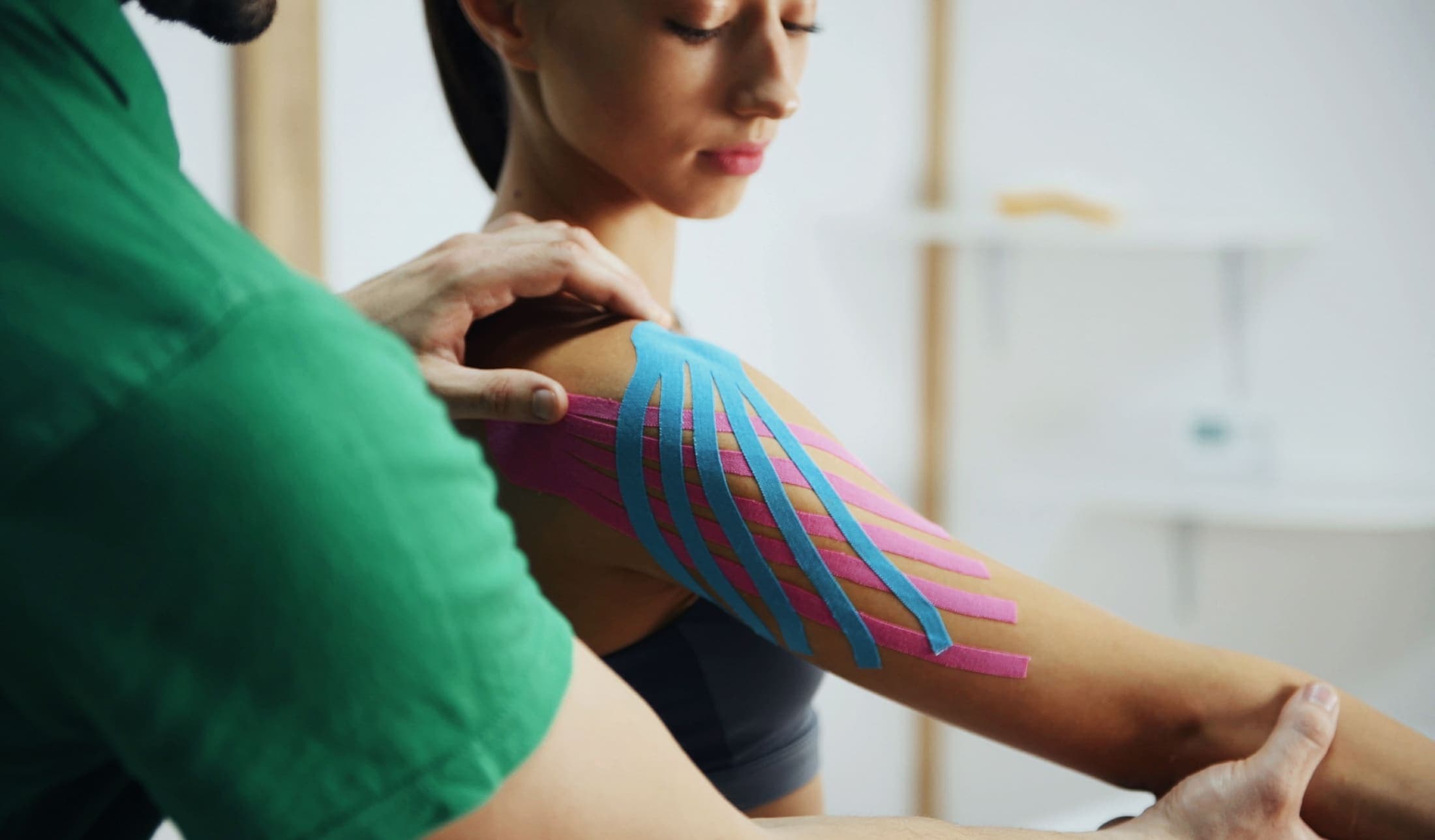 Kinesiotape wordt aangebracht op de schouder tijdens een behandeling.